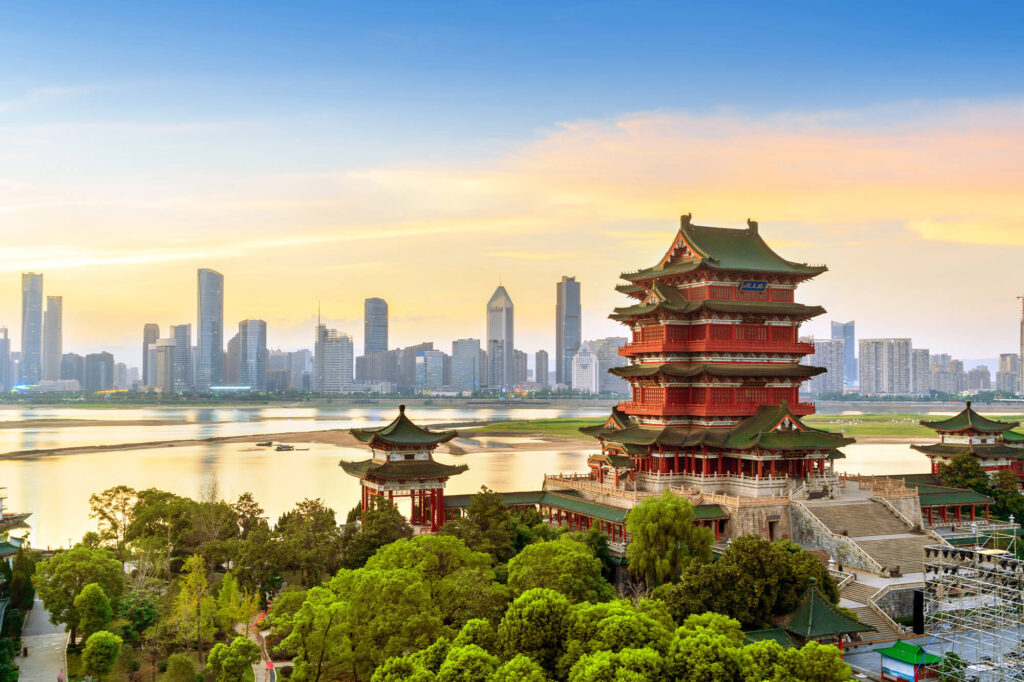 Traditional multi-story Chinese pagoda in foreground with modern urban skyline across a river at sunset