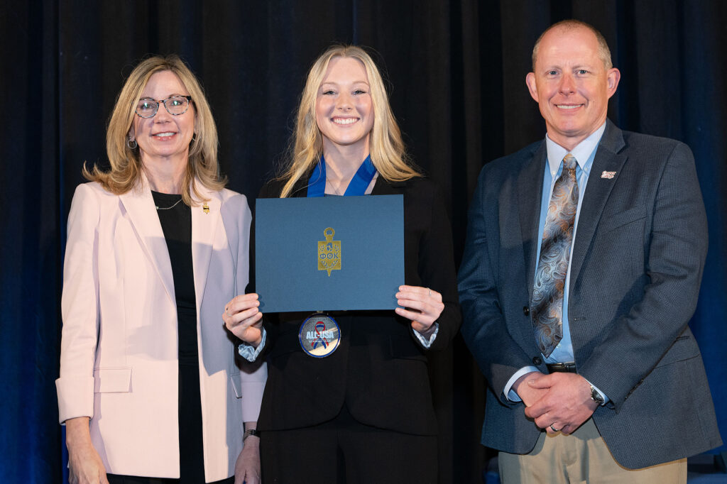 A PTK representaive, Ahnya Ivie-Moody, and Dr. Brandon Kosine holding a Phi Theta Kappa certificate and wearing an All-USA Academic Team medal.