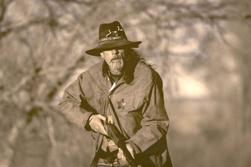Bearded frontiersman in wide-brimmed hat holding rifle from the HOLE IN THE WALL documentary.